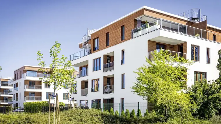 Modernes Mehrfamilienhaus mit Holzverkleidung und Bäumen im Garten